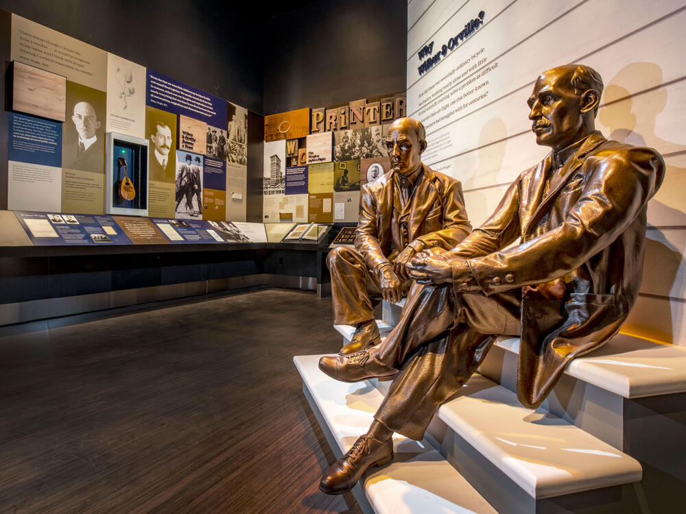 Two bronze statues sitting on steps at the entrance of a museum exhibit. 