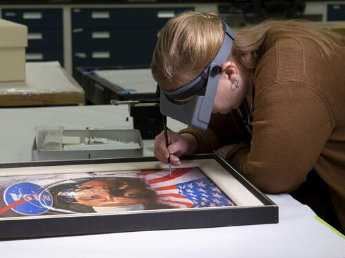 A woman leans over a painting.