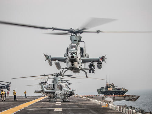 A pale gray Viper helicopter gunship, bristling with weapons pods, lifts off the USS Boxer.