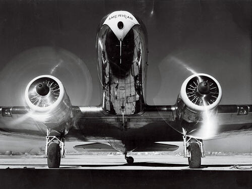 Head-on view of an American Airlines DC-3 airplane, a large passenger airplane, on the ground with its propellers turning. 