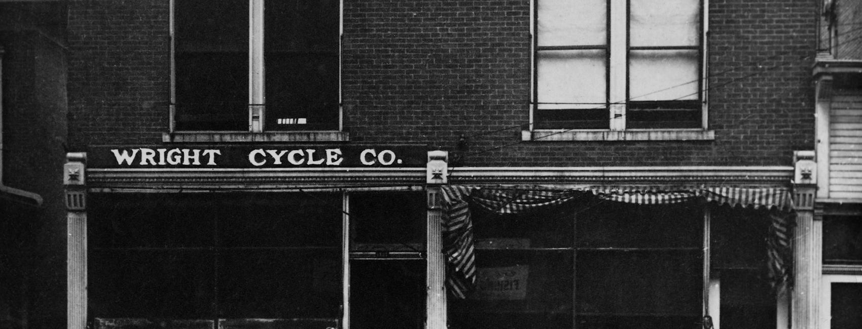 A brick, two-story bulding with a sign on a front facade labeling the building as "The Wright Cycle Co."