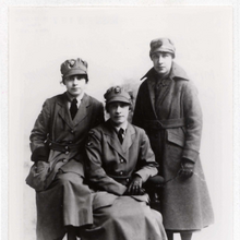 Three women pose for a photo. One sits in front while the two others flank her on either side. They are all wearing military uniforms.